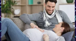 A man and a pregnant woman sitting together on a couch, both smiling warmly and hoping to have twin babies
